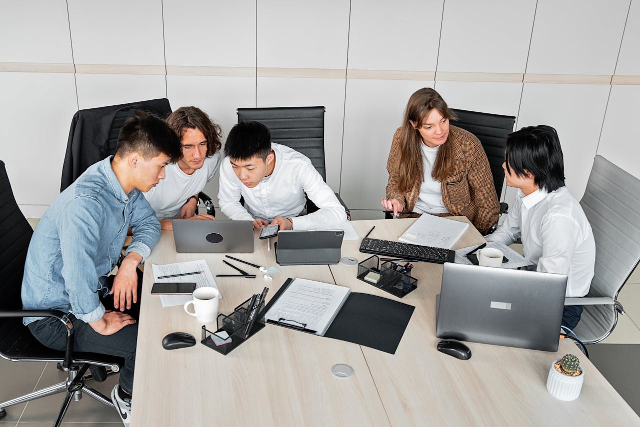 A diverse group of colleagues working together in an office setting with laptops and documents.